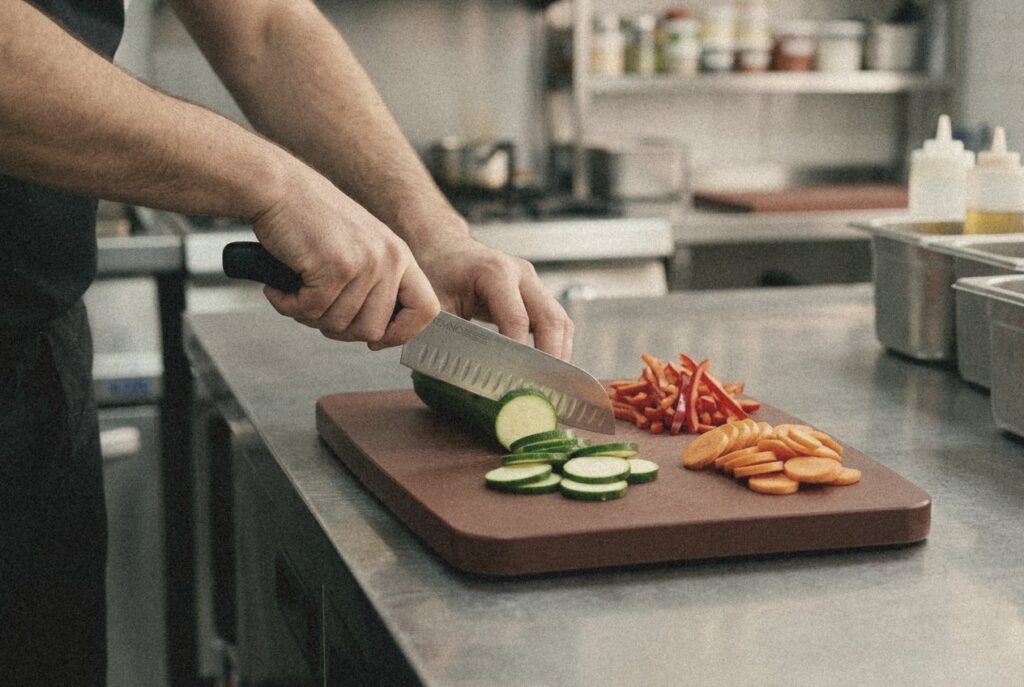 Μαχαίρι santoku TEMNO κόβει κολοκυθάκι σε καφέ πλάκα κοπής